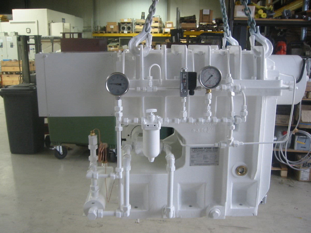Das weiß gefärbte und lackierte Doppelschneckenextruder Getriebe hängt an einem Haken in der Fertigungshalle der Firma KACHELMANN GETRIEBE GmbH. Im Hintergrund sind Werkzeuge und Regale zu erkennen. KACHELMANN GETRIEBE GmbH